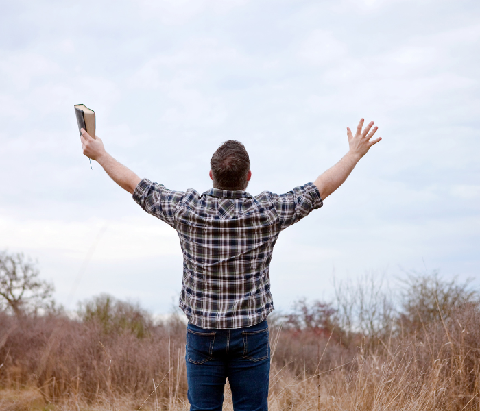 man lifting his arms in praise holding a bible
